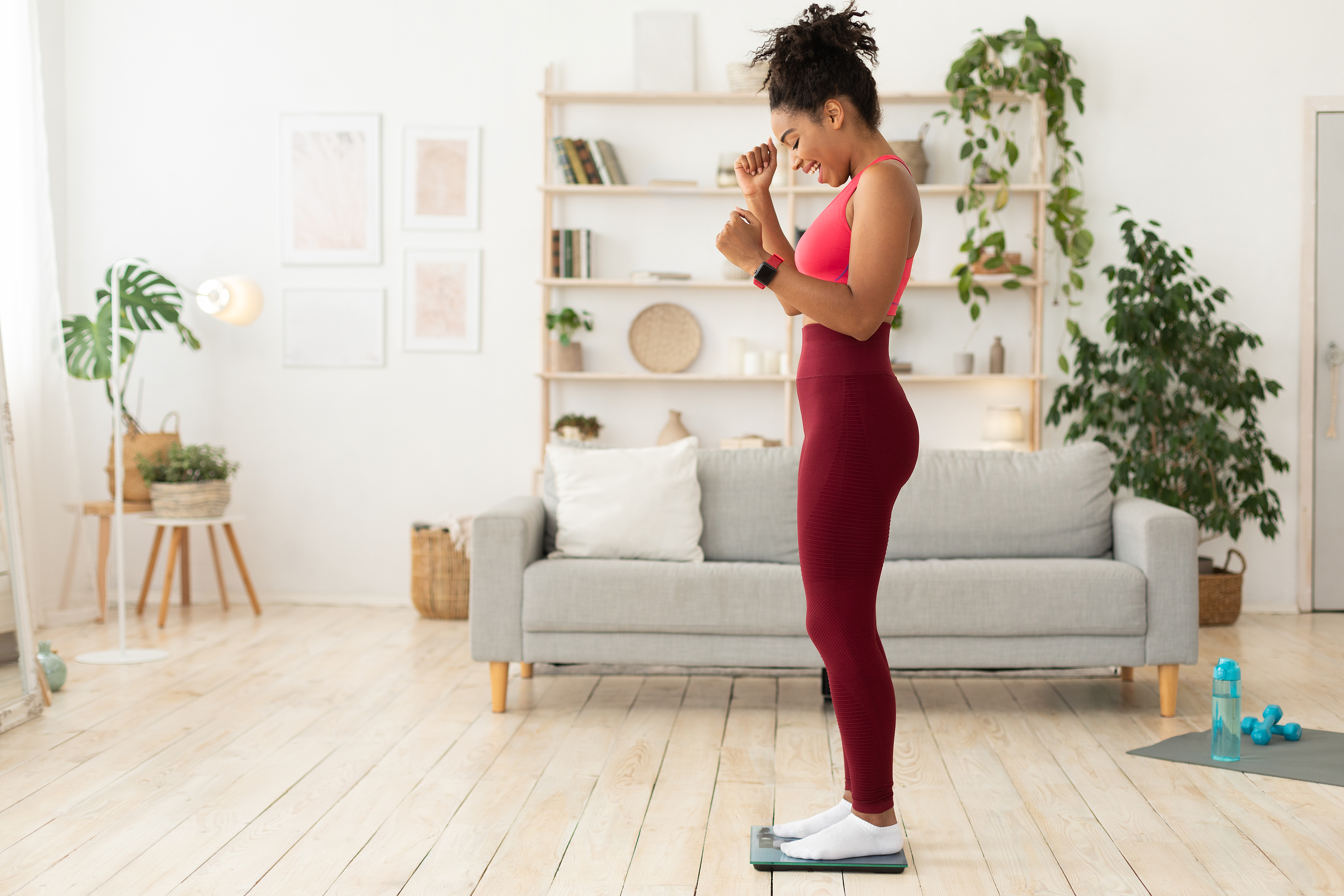 Joyful woman in athletic wear celebrating her progress while standing on a scale at home
